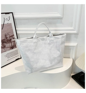 Detail of embossed TOTE BAG text on white waterproof Tyvek shoulder bag with creased texture