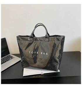 Glossy black waterproof tote bag with white TOTE BAG text in a modern office setting