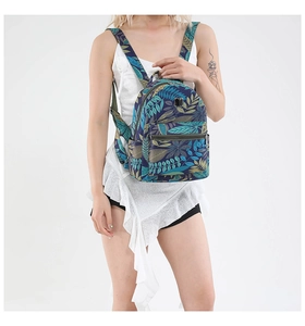 Back view of a mini tropical leaf print backpack worn by a model in a white dress
