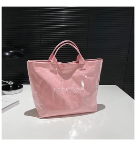 Pink tote bag detail with glossy transparent PVC finish and white TOTE BAG text print