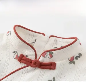 Detail of girls qipao dress showing red frog button and fruit floral embroidery