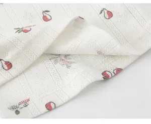 Detailed macro view of white pointelle cotton fabric with red cherry print and neat stitching