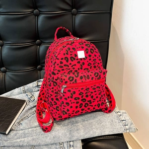 Urban style red leopard print canvas backpack with multiple zipper pockets on a black sofa