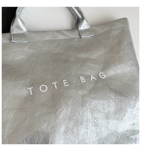 Detail of silver metallic Tyvek tote bag with printed TOTE BAG text and crinkled texture