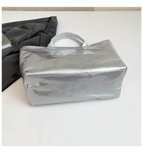 Detail of silver metallic tote bag featuring white TOTE BAG text and a reflective finish