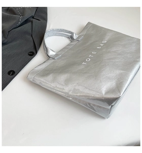 Detail of silver metallic tote bag with letter print against white background