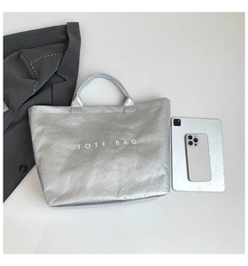 Flat lay of silver metallic tote bag with white TOTE BAG print beside tablet and suit jacket