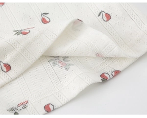 Close-up of white jacquard fabric with cherry print and detailed stitching on the edge