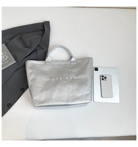 Silver metallic tote bag with printed text showing capacity relative to tablet and phone