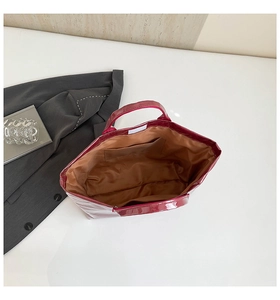 Detail view of dark red glossy patent leather tote bag with brown fabric lining and inner pocket