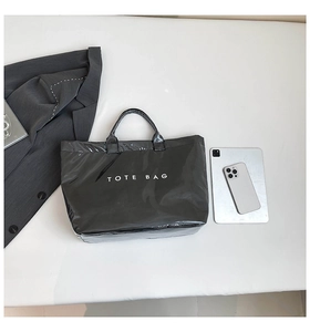 Close-up of black glossy waterproof tote bag featuring white TOTE BAG text in a minimalist style