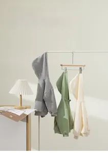Trois vestes à capuche pour enfants en gris, vert et beige sur un cintre blanc élégant
