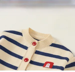 Detail of a beige striped knit cardigan featuring a round neck and red penguin patch
