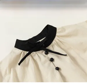 Detail of girls beige blouse featuring contrast black stand collar and cute bow tie