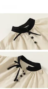 Detail of girls' beige textured blouse with black bow tie and contrast collar