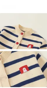 Detail of girls' striped knit cardigan showing red buttons and a cute penguin patch