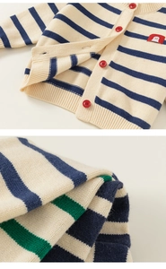 Detail of baby knit cardigan showing red buttons and cute penguin embroidery on striped fabric