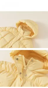 Detail of light yellow hooded down jacket with smooth zipper and silver metal buttons