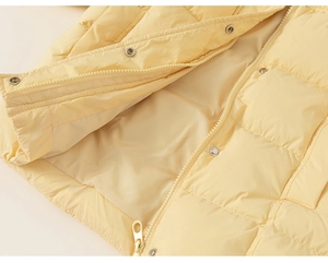 Detail of light yellow quilted down jacket with square texture and metal snap buttons