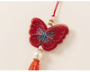 Detailed view of red fabric butterfly ornament with intricate embroidery and white pearl