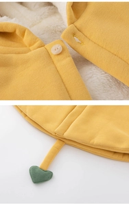 Détail de cape en tricot jaune avec doublure polaire blanche et breloque coeur verte