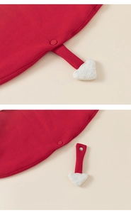 Détail d'une cape en tricot rouge pour bébé avec charm cœur blanc amovible et boutons-pression