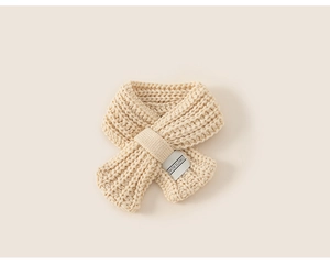 Dettaglio di sciarpa in maglia beige per bambini con fibbia a croce ed etichetta in tessuto