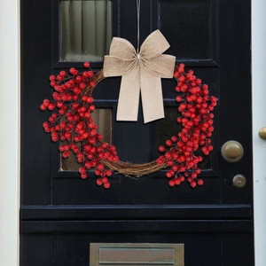 Close-up of a Christmas berry wreath with a linen bow hanging on a black wooden door