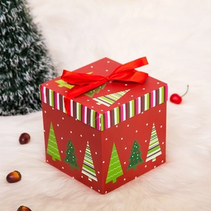 Caja de regalo de Navidad roja con patrones de árboles y lazo de satén en alfombra suave