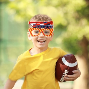 Boy wearing construction crane party glasses on grass with a football outdoors