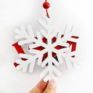 Hand holding a 2024 wooden snowflake ornament with red and white layered design