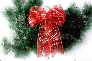 Detail of red organza Christmas bow with gold Merry Christmas print on pine branches
