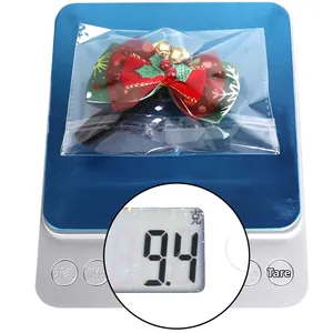 Christmas pet bow tie with holly leaves and bell, weighing 9.4g on a digital scale