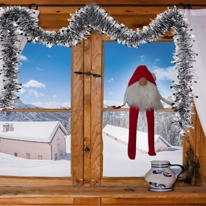 Close-up of a festive long-legged Christmas gnome with silver star tinsel on a window sill