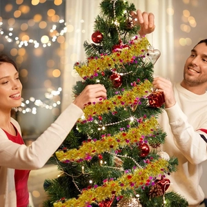 Golden Christmas tinsel garland with stars being decorated on a tree in a cozy home