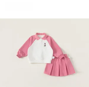 Close-up of pink and white polo shirt with cartoon bear embroidery and pleated skirt