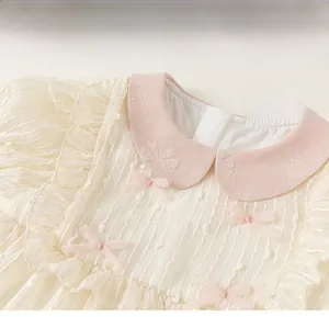 Detail of baby girl dress with pink Peter Pan collar, ruffles and bow in cream chiffon