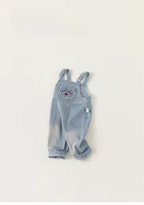Close-up of heart cherry embroidery and metallic buckles on blue denim overalls