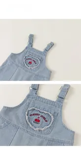 Detail of denim overalls with heart-shaped pocket and red cherry embroidery