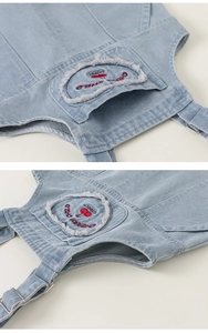 Close-up of light blue denim overalls with cherry embroidery and metal hardware details