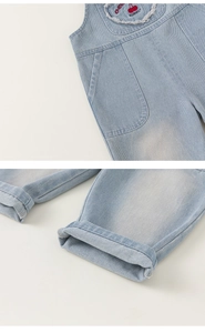 Detail of cherry embroidery on denim overalls with a focus on the cuffed leg hem