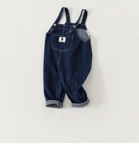 Detail of dark blue denim overalls for toddlers featuring pocket accents and metal buttons