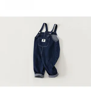 Detail of dark blue denim kids overalls featuring a front pocket and metal buckles