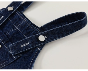 Detail of dark blue denim overalls featuring white stitching and silver metal button