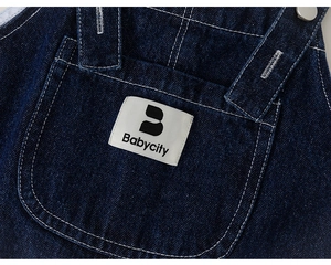 Detail of dark blue denim overalls featuring contrast stitching and a white fabric logo tag