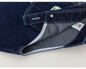 Detail of dark blue denim overalls with white stitching, metal snaps and size label