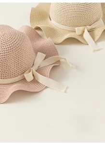 Dettaglio di cappelli di paglia intrecciati a traforo con delicati nastri a fiocco rosa e beige