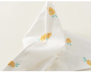 Détail macro d'un bavoir en coton pour bébé avec motifs carottes et ourlet soigné