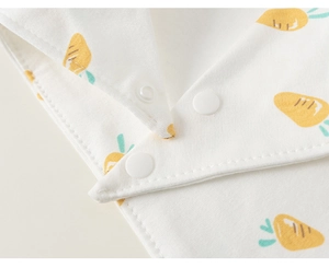 Détail d'un bavoir bébé en coton avec imprimé carotte et trois boutons-pression blancs