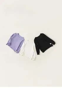 Dettaglio di maglie a maniche lunghe per bambini con bordi a volant in viola, bianco e nero